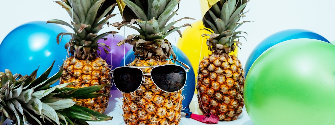 Multiple balloons in different colors, pineapples wearing party hats, and sunglasses.